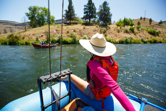 A woman sits on the edge of a raft while drifting by anglers along the Deschutes River in Oregon.