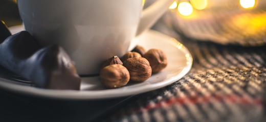 Conceptual photo of a cup of hot tea with nuts in warm colors with Christmas lights, banner