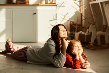 A portrait  of mom and daughter laying on the ray of sun in the pajamas in the kitchen