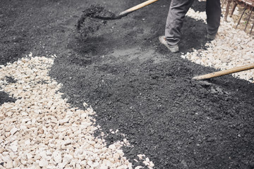 Laying new asphalt, covering the pit, on the rubble. Workers carry in shovels and using asphalt lute for smooth, hot asphalt.