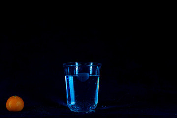 glass of water and orange on black background