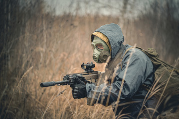 Fototapeta premium Soldier with airsoft rifle in raincoat and gas mask outdoor.