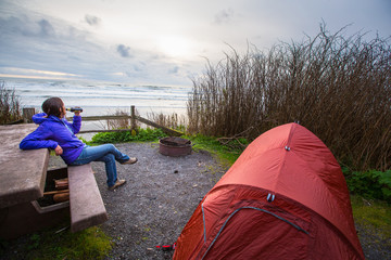 A woman sits on a picnic table with a beer while car camping at a beach side camp site in Kalaloch Campground in the Olympic National Park in Washington State.