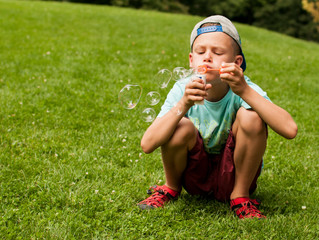 Boy sits in the grass and makes soap bubbles