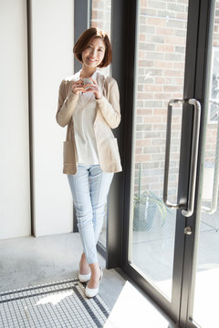 ドア付近に立つマグカップを持った笑顔の20代女性
