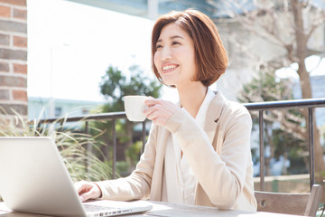 テラス席でパソコンを操作する笑顔の20代女性