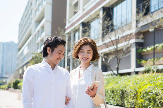 屋外で1台のスマホを見る笑顔の男女