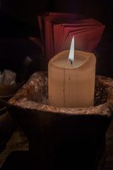Big candle in a plate on a wooden table. Interior lighting with candles. Romantic interior in the dark.