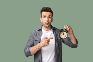 Handsome young man with alarm clock on color background