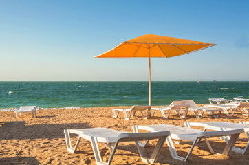 Seascape with sandy beach, umbrella and deck chairs.