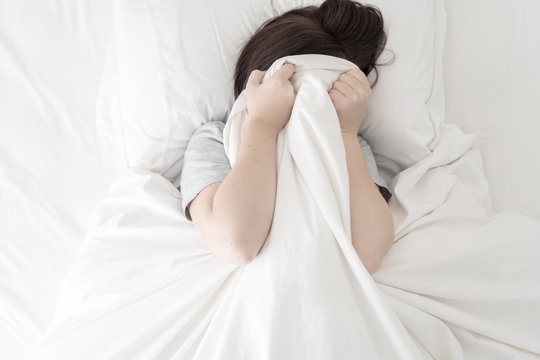 Woman Hiding Her Face Under A Blanket In Bed
