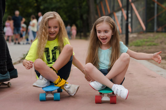 little cute girls with sunglasses and cap sitting on a skateboard. photo of cute preteen girl with skateboard outdoors.