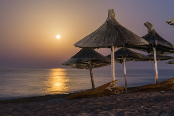 Reed umbrellas with moon over sea