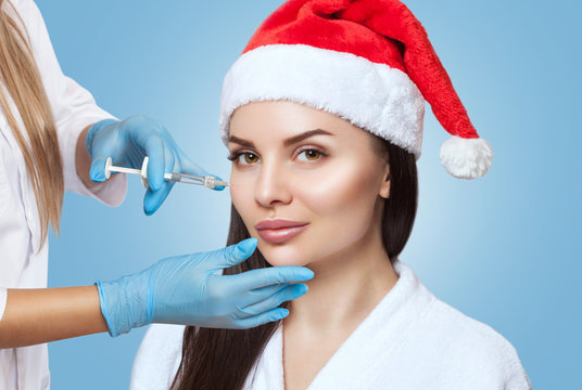 Cosmetologist does prp therapy on the face of a beautiful woman in a Santa Claus hat.New Year's and Cosmetology concept.