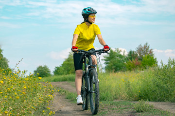 Fototapeta na wymiar Beautiful girl in yellow riding a bike in nature. Sports and recreation. Hobbies and health.