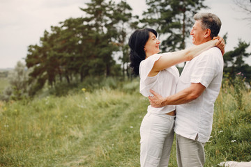 Adult couple in a summer field. Handsome senior in a white shirt. Woman in a white blouse
