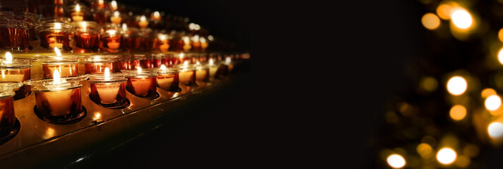 Candles in a church, cathedral or temple, in yellow transparent candlesticks. The concept of mourning. We remember, we grieve. Selective focus, side view, copy space. Banner