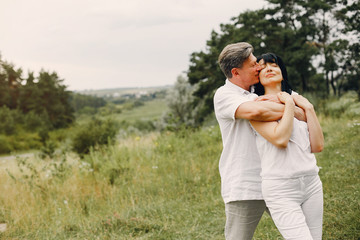 Adult couple in a summer field. Handsome senior in a white shirt. Woman in a white blouse