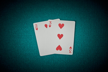 Cards of two and three from hearts on a green poker game mat. Superior view.