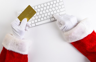 High angle closeup of Santa Claus hands using his computer keyboard to make an online purchase, with his credit card in one hand.