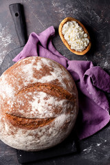 Bread on cutting board and purple cotton napkin and cream cheese in wood plate on dark background top 