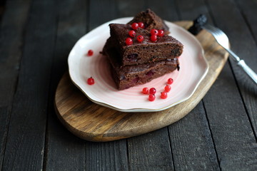 chocolate cake with prunes and cranberries on a dark wooden background.