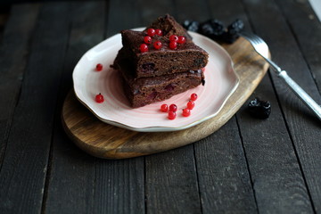 chocolate cake with prunes and cranberries on a dark wooden background.