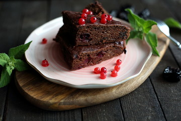 chocolate cake with prunes and cranberries on a dark wooden background.