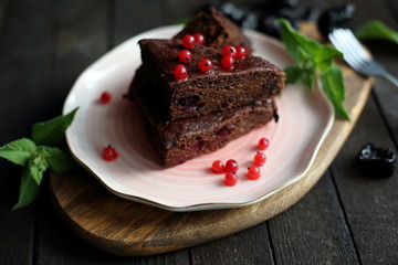 chocolate cake with prunes and cranberries on a dark wooden background.