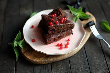 chocolate cake with prunes and cranberries on a dark wooden background.