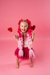 little girl with braids of pink kanekalon holds a heart-shaped Lollipop on a pink background. refusal of sweets. the concept of Valentine's day