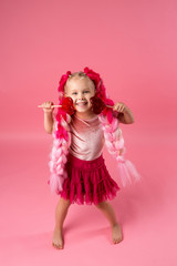 little girl with braids of pink kanekalon holds a heart-shaped Lollipop on a pink background. refusal of sweets. the concept of Valentine's day