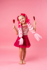 little girl with braids of pink kanekalon holds a heart-shaped Lollipop on a pink background. refusal of sweets. the concept of Valentine's day