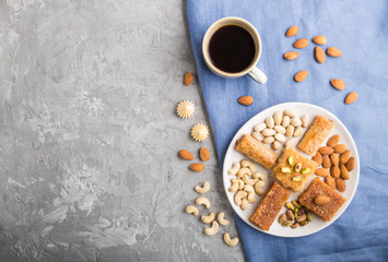 traditional arabic sweets (basbus, kunafa, baklava), a cup of coffee and nuts on a gray concrete background  top view, copy space.