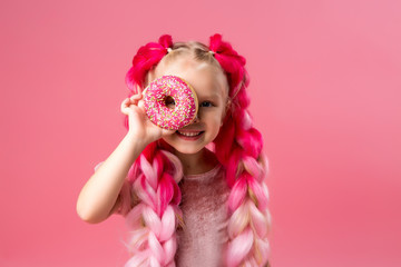 cute little girl in a pink dress with pink braids from kanekalon holds donuts in pink glaze in her hands