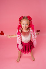 little girl with braids of pink kanekalon holds a heart-shaped Lollipop on a pink background. refusal of sweets. the concept of Valentine's day
