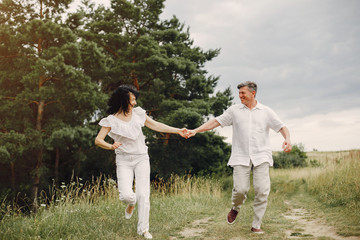 Naklejka na ściany i meble Adult couple in a summer field. Handsome senior in a white shirt. Woman in a white blouse