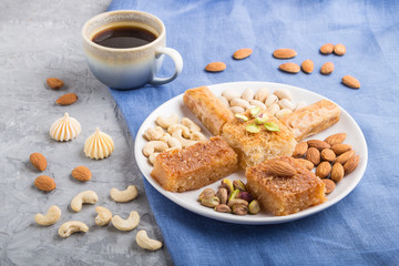 traditional arabic sweets (basbus, kunafa, baklava), a cup of coffee and nuts on a gray concrete background  side view, close up.