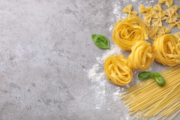 Flat lay composition with different types of pasta on grey background. Space for text