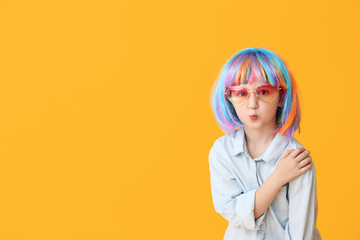 Cute little girl in bright wig on color background