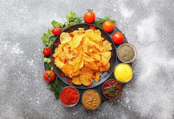 Plate with tasty potato chips, tomatoes and spices on table