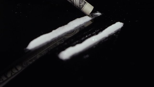 Rack focus of cocaine getting snorted up with a dollar bill on a mirrored surface 