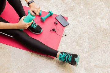 Stock photo of a young woman resting after exercising at home in the living room with a bottle