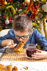 Chłopiec z otwartą buzią podczas jedzenia obiadu. Nakłada do buzi duży kawałek pysznej potrawy. Święta |Bożego Narodzenia. - obrazy, fototapety, plakaty