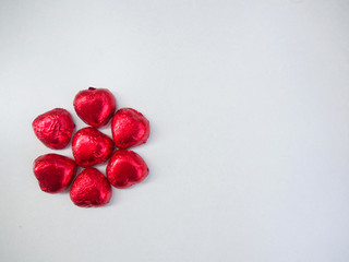 The chocolate is wrapped by red paper in heart shape that placed on the white background. 