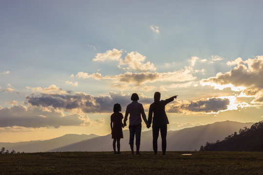 Group of children and woman stands on mountain top and looks at sunset.