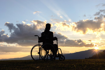 Fototapeta na wymiar Disabled handicapped woman is sitting on wheelchair at sunset.