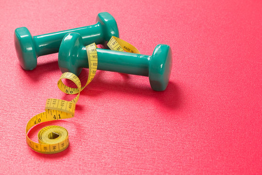 Stock photo of two dumbbells and a measuring tape on an exercise mat