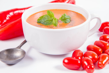 Gazpacho soup with some tomatoes and sweet pepper , decorated with fresh mint and black pepper on a white background with a vintage spoon