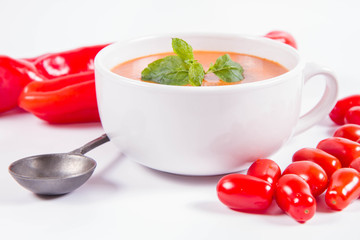 Gazpacho soup with some tomatoes and sweet pepper , decorated with fresh mint and black pepper on a white background with a vintage spoon